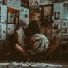 "A reflective basketball player sitting in a room filled with magazine clippings, holding a worn basketball."